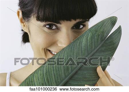 "Young woman holding leaf in front of face, smiling, portrait" View Large Photo Image Stock Photograph - "Young woman holding leaf in front of face, smiling, portrait". Fotosearch