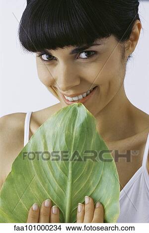 Picture - "Young woman holding leaf, smiling, portrait". Fotosearch