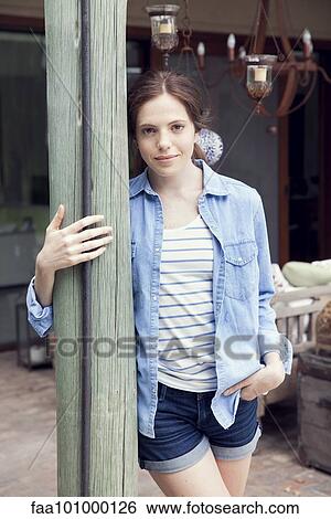 Stock Photograph - "Young woman leaning against wooden post, portrait". Fotosearch