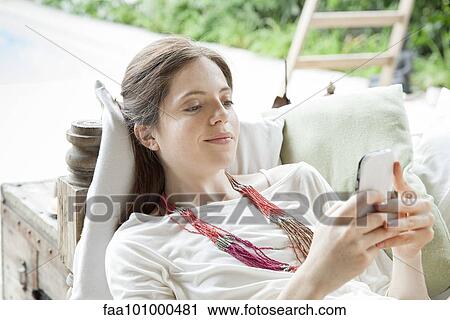 "Young woman lying on back, using smartphone outdoors" View Large Photo Image Stock Image - "Young woman lying on back, using smartphone outdoors". Fotosearch