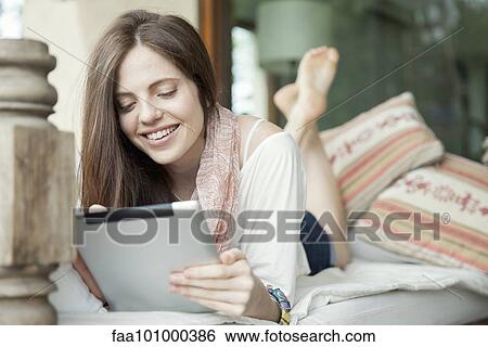 Young woman lying on stomach using digital tablet View Large Photo Image Stock Photograph - Young woman lying on stomach using digital tablet. Fotosearch