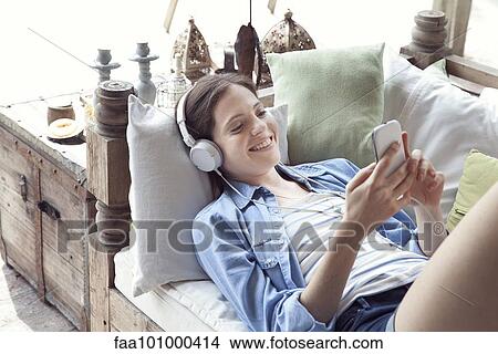 Picture - Young woman relaxing with smartphone and headphones. Fotosearch