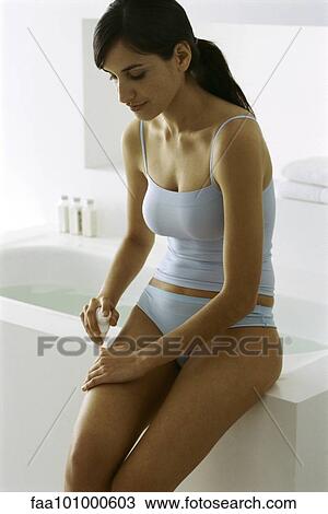"Young woman sitting on edge of bathtub, putting moisturizer on leg" View Large Photo Image Stock Image - "Young woman sitting on edge of bathtub, putting moisturizer on leg". Fotosearch