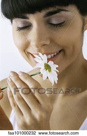 Stock Image - "Young woman smelling flower, smiling, eyes closed". Fotosearch