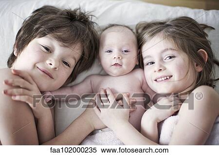 Stock Photography - "Boy and girl lying on bed with baby brother, portrait". Fotosearch