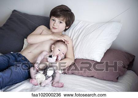 Boy resting on bed with baby brother View Large Photo Image Stock Photograph - Boy resting on bed with baby brother. Fotosearch