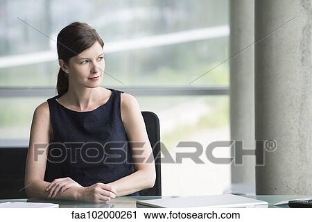 Stock Image - Business executive at desk looking away contemplatively. Fotosearch