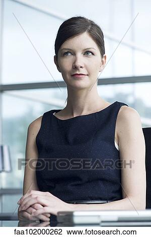 "Businesswoman sitting at desk, looking away in thought, portrait" View Large Photo Image Stock Image - "Businesswoman sitting at desk, looking away in thought, portrait". Fotosearch