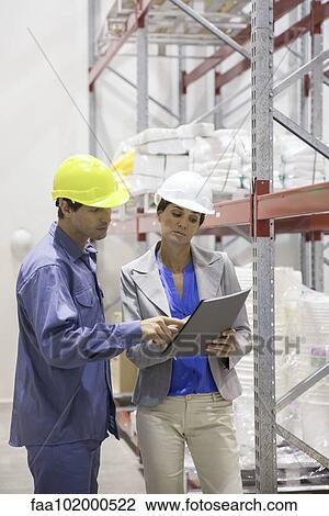 Stock Image - Colleagues discussing plan at warehouse. Fotosearch