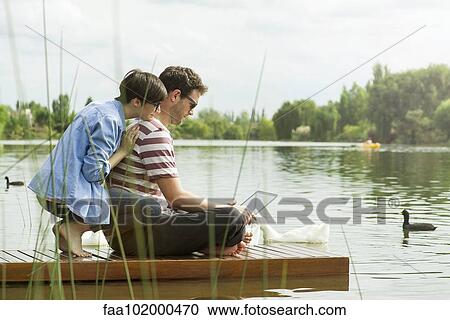Stock Image - Couple using laptop computer on dock. Fotosearch