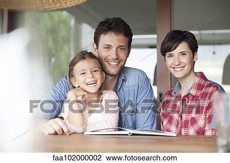 Stock Image - "Family sitting together at table with open book, portrait". Fotosearch
