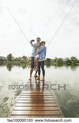 Family with young daughter standing together at end of lake pier taking selfie View Large Photo Image Stock Image - Family with young daughter standing together at end of lake pier taking selfie. Fotosearch