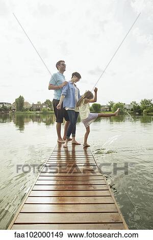 Stock Photo - Family with young daughter standing together at end of lake pier. Fotosearch