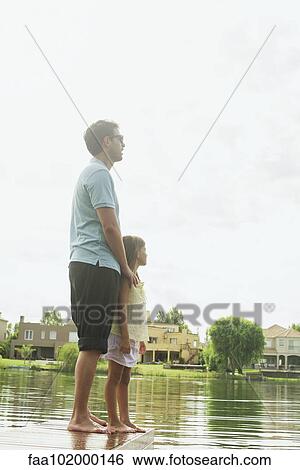 Father and daughter standing together at end of lake pier looking at view View Large Photo Image Stock Photograph - Father and daughter standing together at end of lake pier looking at view. Fotosearch