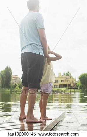 Father and daughter standing together at end of lake pier looking at view View Large Photo Image Stock Photography - Father and daughter standing together at end of lake pier looking at view. Fotosearch