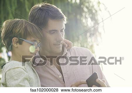 "Father and son looking at smartphone outdoors, overexposure" View Large Photo Image Stock Photo - "Father and son looking at smartphone outdoors, overexposure". Fotosearch