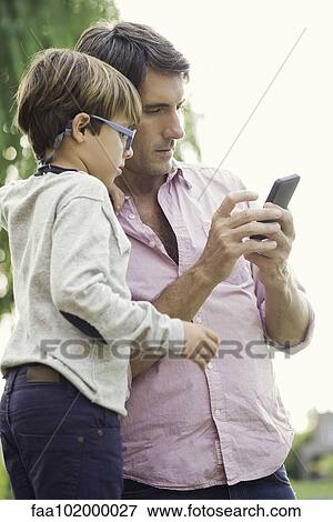 Stock Photo - Father and young son looking at smartphone together outdoors. Fotosearch