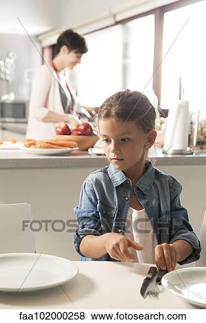 "Girl setting the table, mother preparing food in the background" View Large Photo Image Stock Photo - "Girl setting the table, mother preparing food in the background". Fotosearch