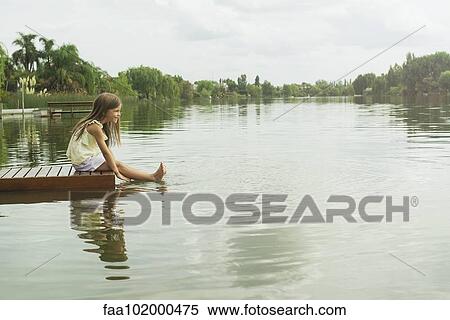 Stock Photography - "Girl sitting on dock with feet dangling in lake, portrait". Fotosearch