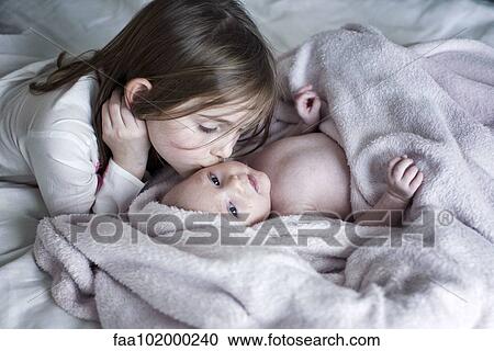 Little girl kissing baby brother's cheek on bed View Large Photo Image Stock Image - Little girl kissing baby brother's cheek on bed. Fotosearch