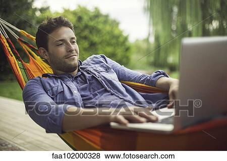Man reclining in hammock using laptop computer View Large Photo Image Stock Photo - Man reclining in hammock using laptop computer. Fotosearch