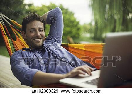 Stock Photo - Man reclining in hammock using laptop computer. Fotosearch