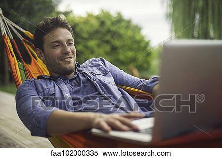 Stock Photography - "Man relaxing in hammock, using laptop computer". Fotosearch