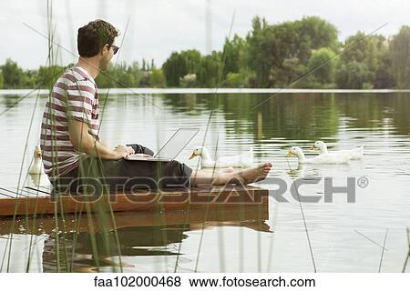 Man sitting on dock using laptop computer View Large Photo Image Stock Photo - Man sitting on dock using laptop computer. Fotosearch