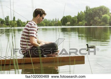 Man sitting on dock using laptop computer View Large Photo Image Stock Photo - Man sitting on dock using laptop computer. Fotosearch