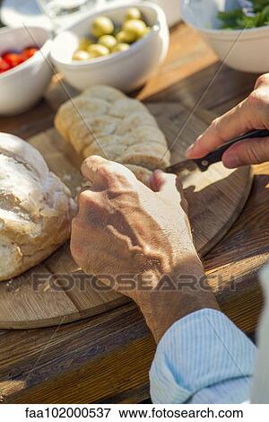 Stock Photo - Man's hands cutting fresh loaf of bread outdoors. Fotosearch