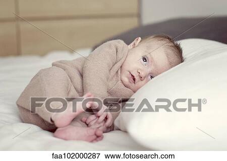Stock Photo - "Newborn baby lying on bed, looking up". Fotosearch
