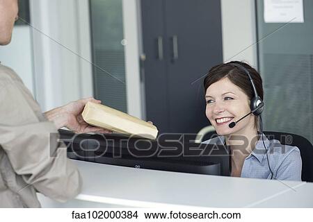 Picture - Receptionist receiving package from delivery person. Fotosearch