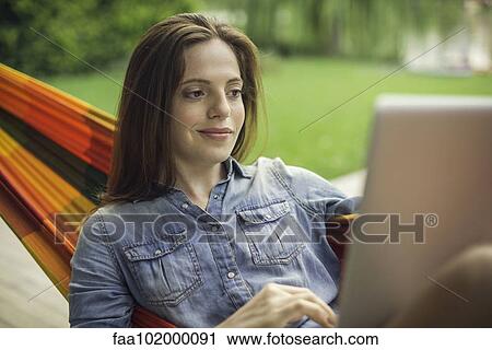 Stock Image - Woman reclining in hammock with laptop computer. Fotosearch