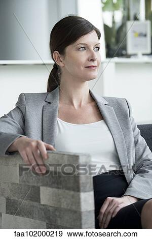Stock Photo - Woman relaxing in arm chair looking away contemplatively. Fotosearch