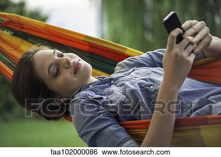 Stock Photograph - Woman relaxing in hammock with smartphone. Fotosearch