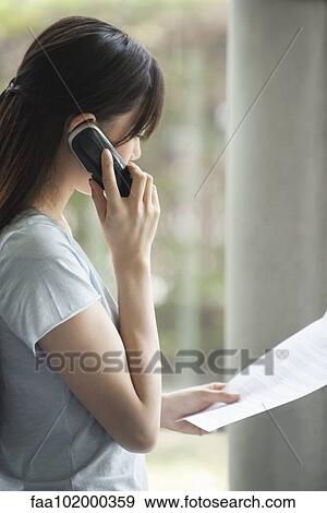 "Woman talking on cell phone, looking at document" View Large Photo Image Stock Photo - "Woman talking on cell phone, looking at document". Fotosearch