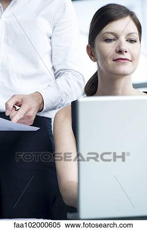 Stock Photography - "Woman working on laptop computer, boss watching over her shoulder". Fotosearch