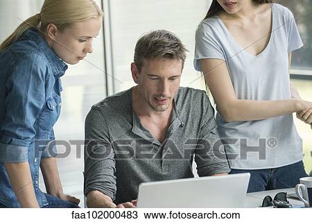 Stock Image - Workers gathered around desk of colleague. Fotosearch