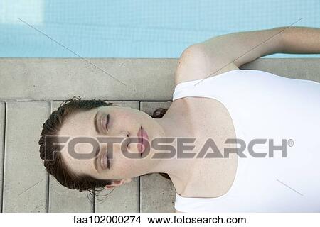 Picture - "Young woman sunbathing by pool with eyes closed, overhead view". Fotosearch