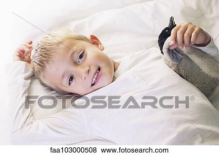 Stock Photo - "Boy lying down with stuffed penguin, portrait". Fotosearch