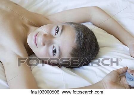 Stock Photograph - "Boy lying on bed, smiling, portrait". Fotosearch