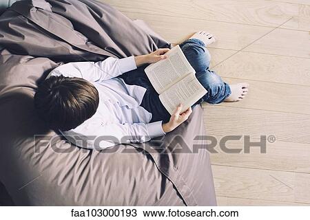 Stock Image - "Boy sitting on beanbag chair, reading book". Fotosearch