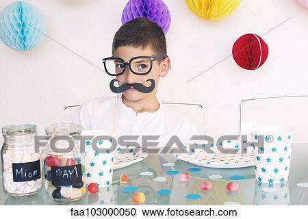Stock Image - Boy wearing fake glasses and mustache at a birthday party. Fotosearch