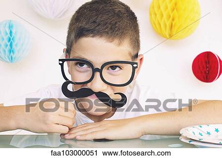 Stock Image - "Boy wearing fake glasses and mustache at a birthday party, portrait". Fotosearch