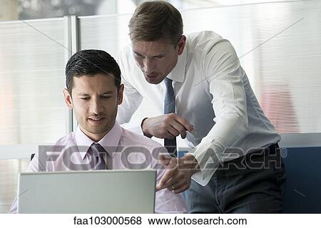 Businessman and colleague looking at computer together View Large Photo Image Stock Photo - Businessman and colleague looking at computer together. Fotosearch