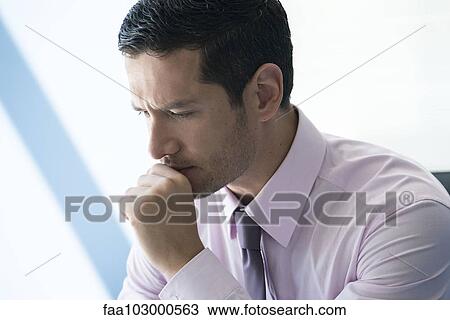 Stock Image - Businessman with hand under chin with look of concern. Fotosearch