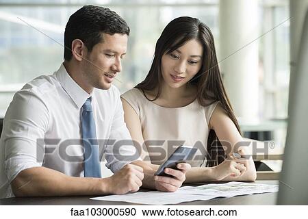 Stock Image - Colleagues looking at smartphone together in office. Fotosearch