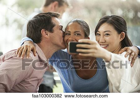 Stock Image - Friends posing for smartphone selfie. Fotosearch