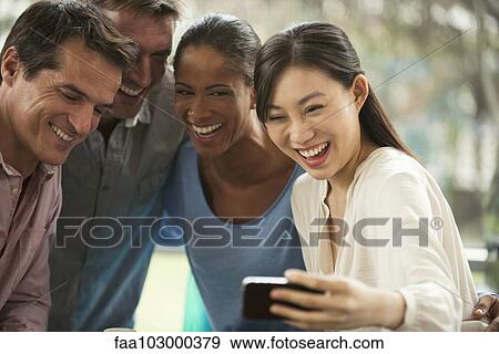 Stock Photo - "Friends posing for smartphone selfie, laughing cheerfully". Fotosearch