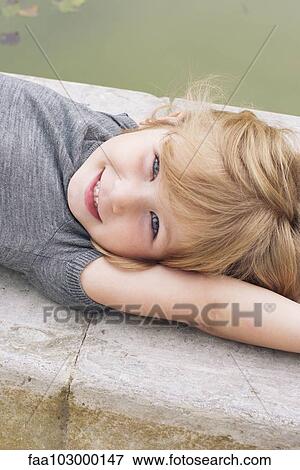 Stock Photo - "Little girl lying beside pond, portrait". Fotosearch